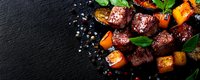 Grilled beef steak cubes with roasted pumpkin, fresh basil leaves and peppercorns on black stone background. Juicy meat appetizer for restaurant menu.