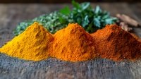 Vibrant piles of turmeric, paprika and chili powder spices on rustic wooden surface with fresh herbs. Natural ingredients for cooking and seasoning food.