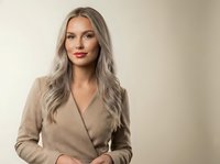 Professional blonde businesswoman in beige blazer sitting confidently in modern office setting for corporate presentations and business communications.