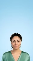 Young woman with dark curly hair and olive complexion wearing sage green v-neck shirt against light blue background. Professional headshot for corporate, medical, or business applications.