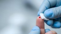 Medical professional in blue gloves performing blood glucose test with lancet device on patient finger for diabetes monitoring and healthcare diagnosis.