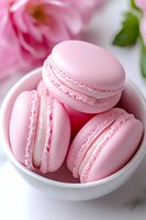 Pink macarons with delicate filling in white ceramic bowl against blurred floral background. Close-up view shows smooth meringue texture and creamy layers.