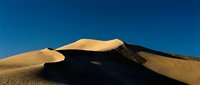Majestic sand dunes with golden slopes and deep shadows under clear blue sky, showcasing desert landscape and natural terrain formations for travel and nature projects.