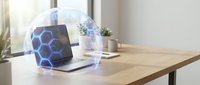 Modern laptop displaying hexagonal network pattern under protective transparent dome on wooden desk in bright office workspace for technology security concepts.
