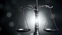 Ornate scales of justice with dramatic lighting against dark background symbolizing law, legal system, and judicial balance in courtroom settings.