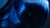 Vibrant electric blue hair flowing in motion against dark background, close-up view showing glossy, silky texture and dynamic movement of styled locks.