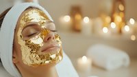 Young woman relaxing with luxury gold leaf facial mask treatment at spa. Soft bokeh lights and white towels create peaceful wellness atmosphere.