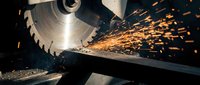 Industrial circular saw cutting metal with bright orange sparks flying in workshop. Manufacturing metalworking process for construction projects.