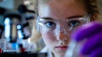 Young female scientist in protective eyewear conducting research in laboratory setting with test tubes and equipment, focused on scientific experiment.