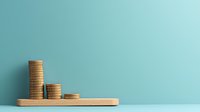 Stacked gold coins arranged in descending order on wooden platform against turquoise wall background, representing financial decline or budget management concept.