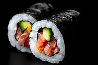 Fresh salmon and avocado sushi rolls with rice and nori on black background, close-up view showing vibrant ingredients and precise preparation technique.