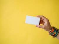 Close-up of a hand holding a blank white card against a bright yellow background, suitable for business card mockups and promotional designs.