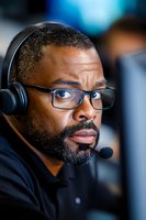 African American male professional wearing headset and glasses in corporate setting, focused expression while communicating during business conference call.