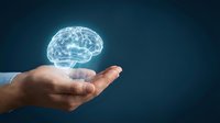 Glowing digital brain hologram floating above open palm against dark blue background representing artificial intelligence, neuroscience and mental health concepts.