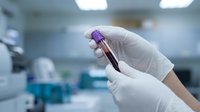 Scientist hand in white latex glove holding blood sample tube in laboratory setting for medical testing, research, and healthcare diagnostics.