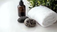Spa wellness composition with volcanic stones, white cotton towel, amber glass bottle and green plant on light background for massage therapy.