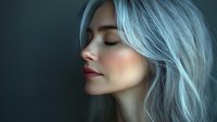 Young Asian woman with blue dyed hair and closed eyes in profile view against dark background, soft lighting creates dreamy atmospheric mood for beauty and fashion concepts.