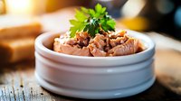 Fresh tuna salad garnished with parsley in white ceramic bowl on wooden surface, soft natural lighting creates appetizing mood for food photography.