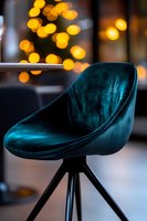 Modern emerald velvet bar stool against blurred golden bokeh lights background creates luxurious atmosphere in contemporary interior setting.