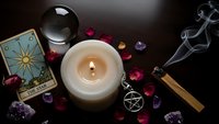 Mystical altar setup with burning candle, tarot cards, crystal ball, amethyst gems, pentagram pendant and sage stick for spiritual rituals and divination practices.