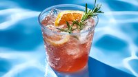 Refreshing summer cocktail with orange slice and rosemary garnish in glass with ice cubes against blue pool water background, cold drink photography.