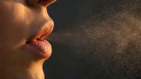 Close-up profile of woman's lips and nose in warm golden sunlight against dark textured background for beauty and skincare concepts.
