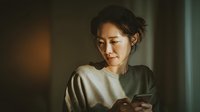 Asian woman using smartphone at home in soft natural light, casual lifestyle moment for communication and technology concepts.