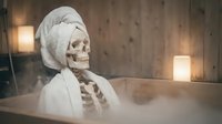 Skeleton wearing white head wrap and draped fabric in modern interior with warm lighting and wooden walls, suitable for Halloween, medical education, or artistic concepts.