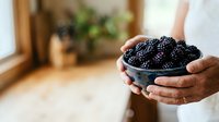 Hands holding bowl of fresh ripe blackberries in bright kitchen setting. Organic fruit harvest and healthy eating concept for food and wellness marketing.