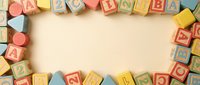 Colorful wooden alphabet blocks arranged in border frame on cream background with copy space for educational content and children learning materials.