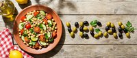 Fresh chickpea salad with tomatoes, cucumber, and herbs on rustic wood, with vegan lettering made from olives for healthy lifestyle content.