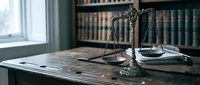 Scales of justice on wooden desk in law office with legal books background. Professional attorney workspace for legal consultation and court proceedings.