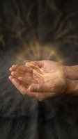 Cupped hands holding glowing golden energy light with magical rays emanating upward against dark background for spiritual healing concepts.
