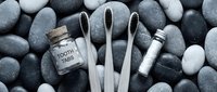 Eco-friendly bamboo toothbrushes with charcoal bristles, tooth tabs jar, and floss on smooth gray pebble background. Zero waste oral care concept.