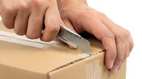 Hands using utility knife to open cardboard box on white background, isolated for design use.