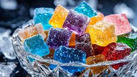 Colorful sugar coated jelly candies in crystal glass bowl with ice cubes. Vibrant gummy sweets with sugar crystals in rainbow colors on dark background.