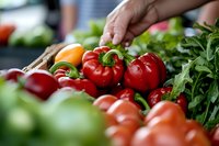 Hand selecting fresh red tomatoes from colorful organic vegetable display at farmers market with green herbs and produce in background for healthy cooking.