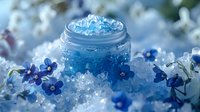 Luxurious blue cosmetic gel with ice crystals in glass jar surrounded by delicate spring flowers and frost creates magical skincare atmosphere.