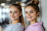 Young Caucasian female twins with hair buns wearing casual hoodies smile confidently at camera, showing natural beauty and positive emotions in modern setting.
