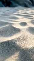 Soft sunlight creates gentle shadows on fine white sand, capturing tranquil beach texture with shallow depth of field for serene coastal atmosphere.