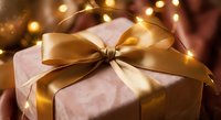Elegant gift box wrapped in soft pink paper with luxurious golden satin ribbon bow, surrounded by warm glowing fairy lights creating festive holiday atmosphere.