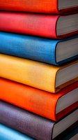 Stack of colorful hardcover books with textured fabric covers in vibrant orange, red, blue, yellow and purple shades against light background. Close-up view shows binding detail.