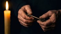 Elderly hands holding vintage key by candlelight in dark atmospheric setting. Concept of mystery, secrets, unlocking memories, heritage and wisdom.