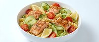 Fresh pasta salad with grilled salmon, cherry tomatoes, cucumber ribbons and herbs in white bowl on clean background for healthy meal concepts.