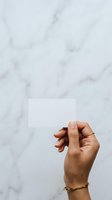 Hand holding blank white card against marble background, ideal for business card mockups, branding presentations, and corporate identity designs.