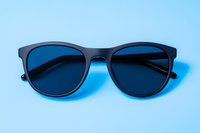 Modern black sunglasses with dark lenses on light blue background. Minimalist fashion accessory photographed from above in studio lighting conditions.