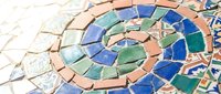 Colorful broken ceramic tile mosaic art with spiral pattern in blue, green and terracotta pieces creating decorative surface texture.