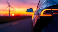 Modern electric car rear light detail against dramatic sunset sky with wind turbine and sun silhouette on rural road, sustainable transportation concept.