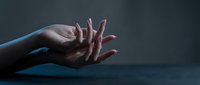 Elegant female hands with manicured nails in graceful gesture against dark moody background for beauty and skincare concepts.