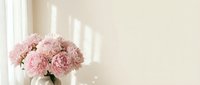 Soft pink peonies in white vase on windowsill with natural sunlight creating gentle shadows on neutral wall background for home decor and lifestyle content.